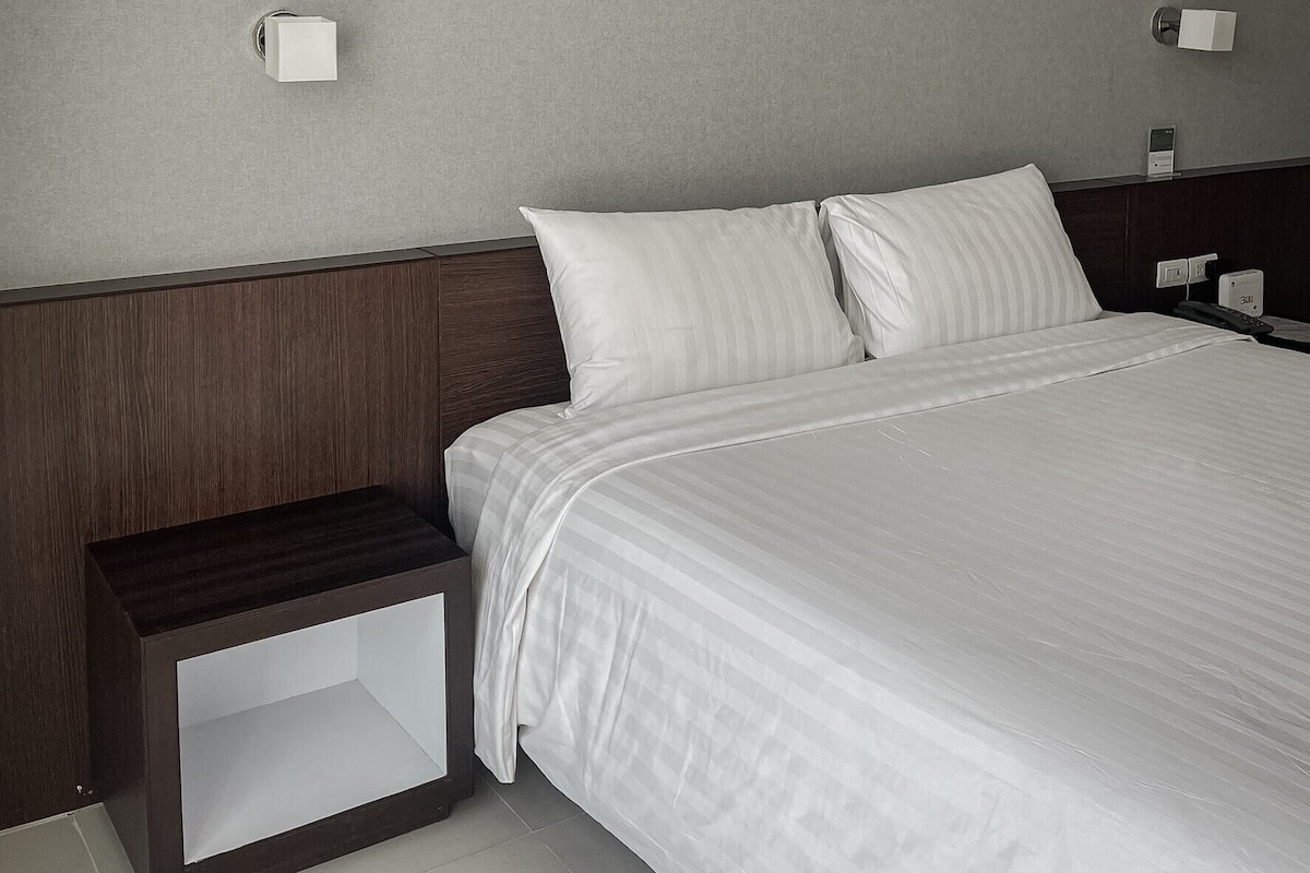 Una habitación de hotel moderna con una cama grande, cabecera de madera y mesitas de noche con lámparas.