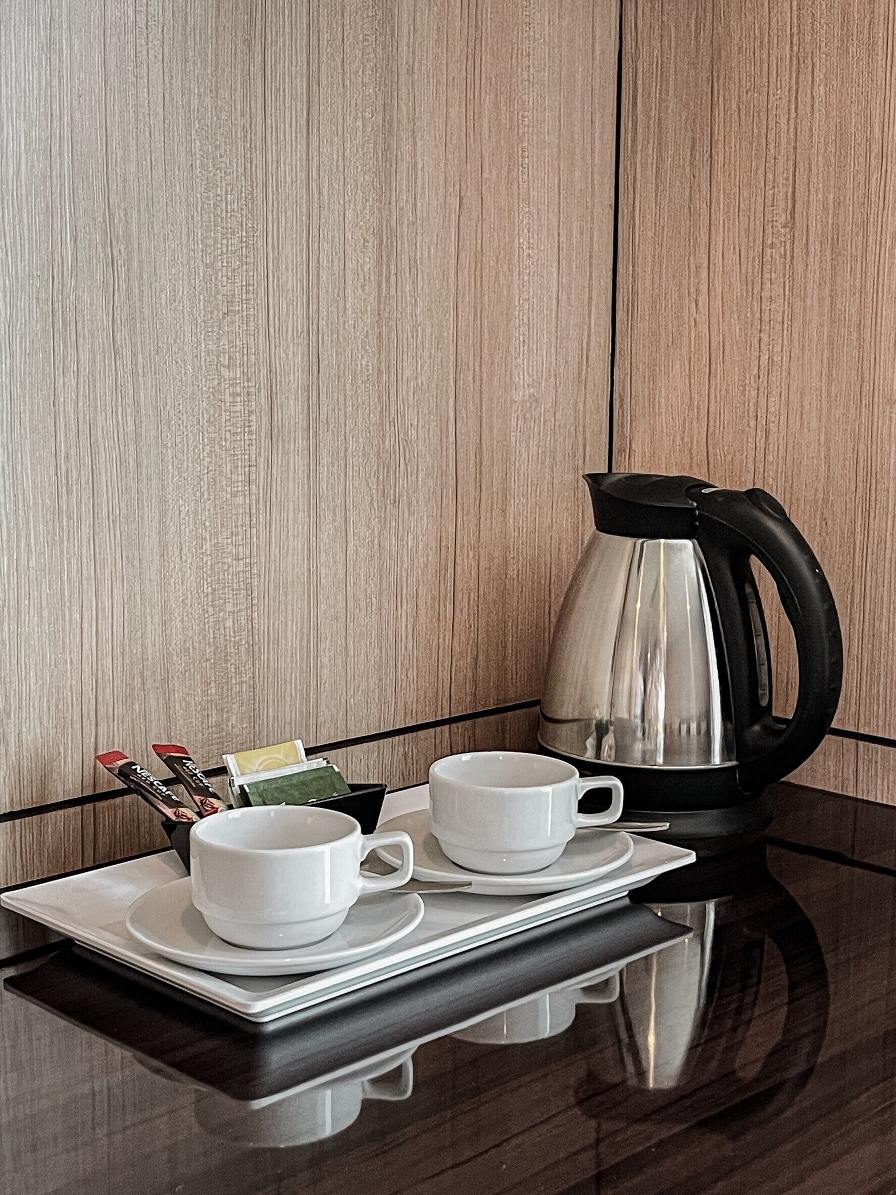 Une table préparée pour le petit-déjeuner, avec une machine à café, deux tasses et un plateau contenant un sachet de thé et des sachets de sucre.
