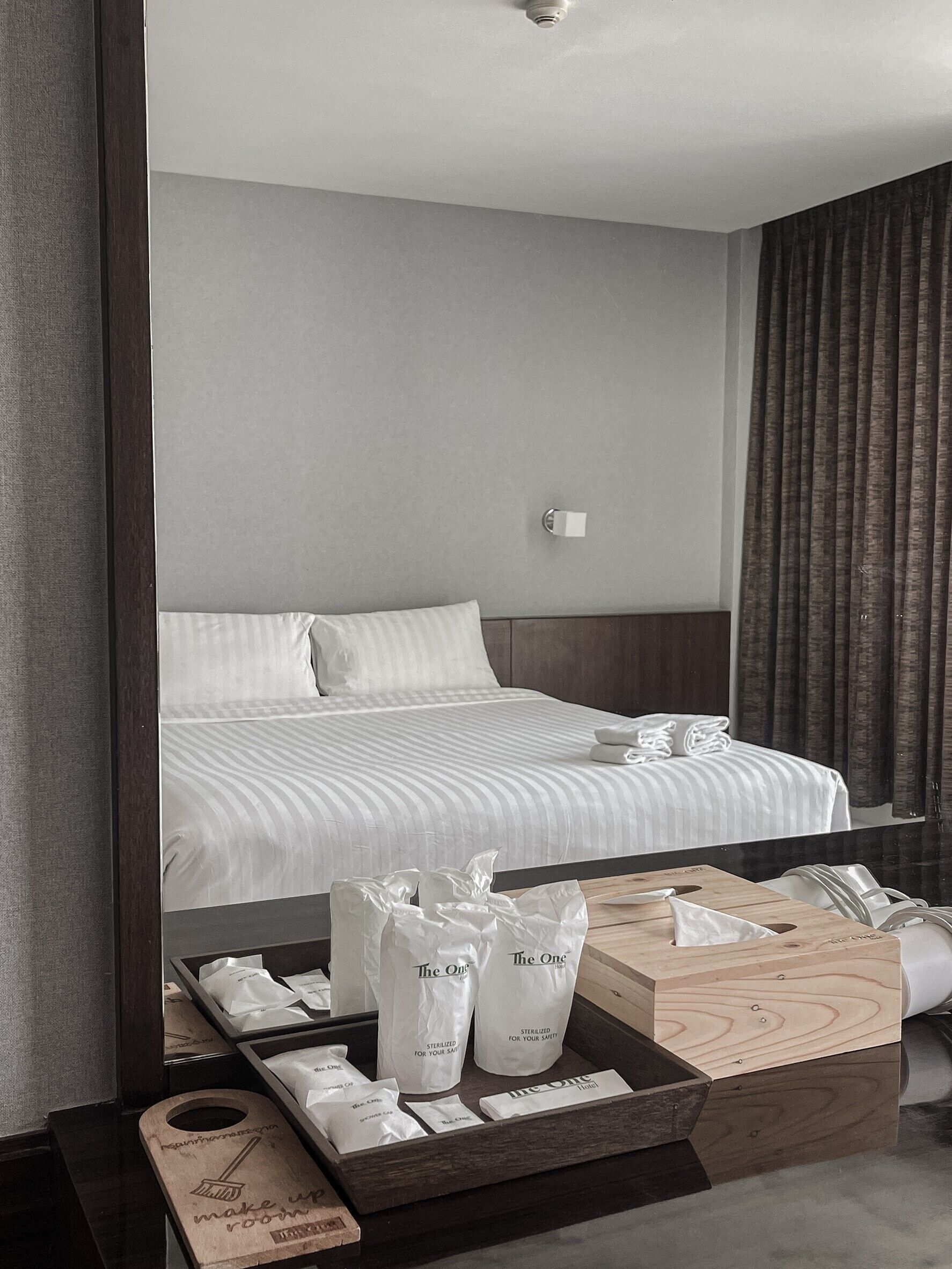A hotel room with a neatly made bed, a bedside table with a tissue box, and a tray with toiletries.
