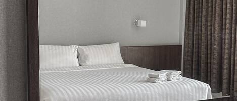 A hotel room with a neatly made bed, a bedside table with a tissue box, and a tray with toiletries.