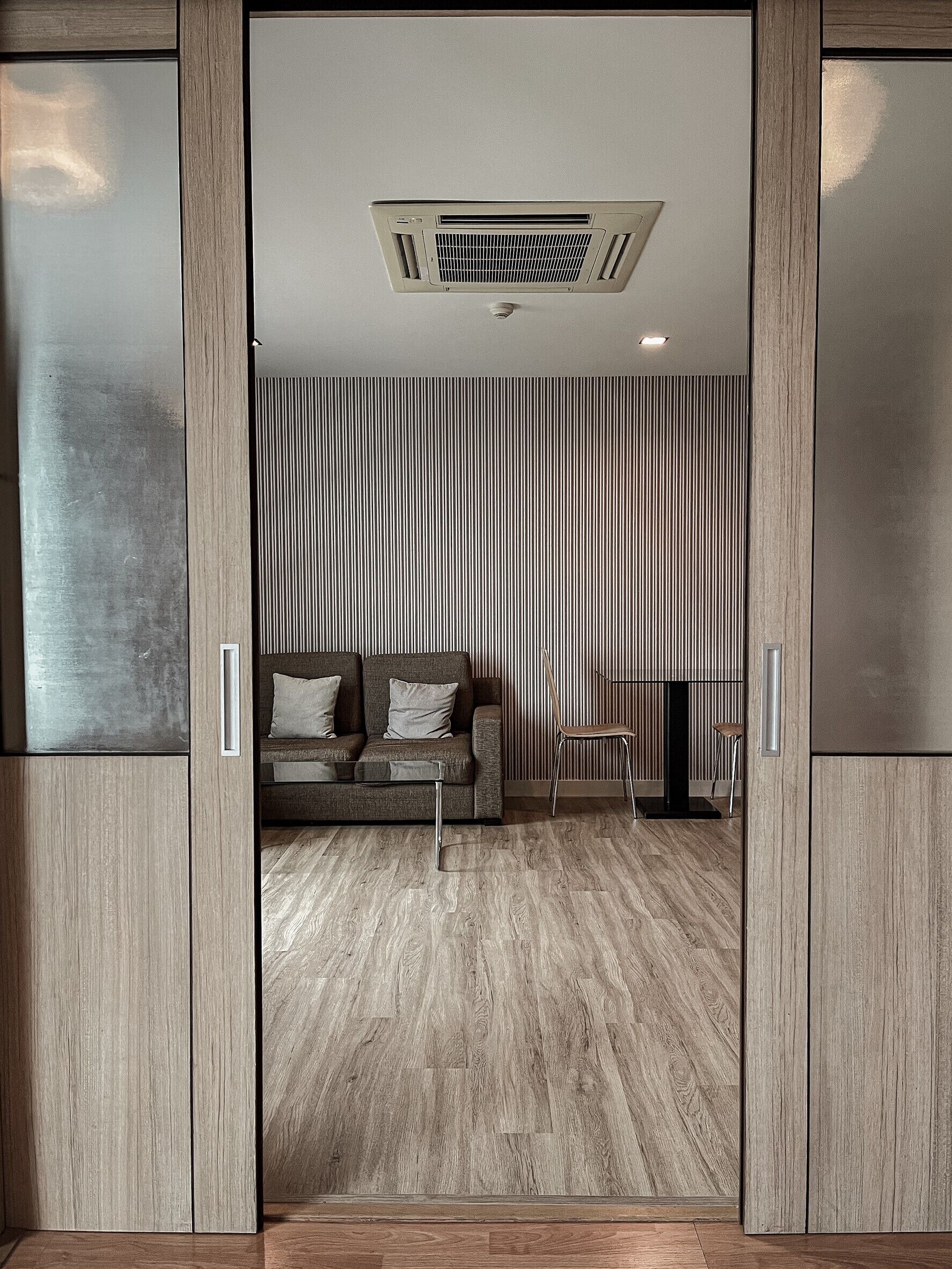 Una sala de estar moderna con un sofá, una mesa de centro y una silla. Presenta una pared a rayas y una rejilla en el techo.
