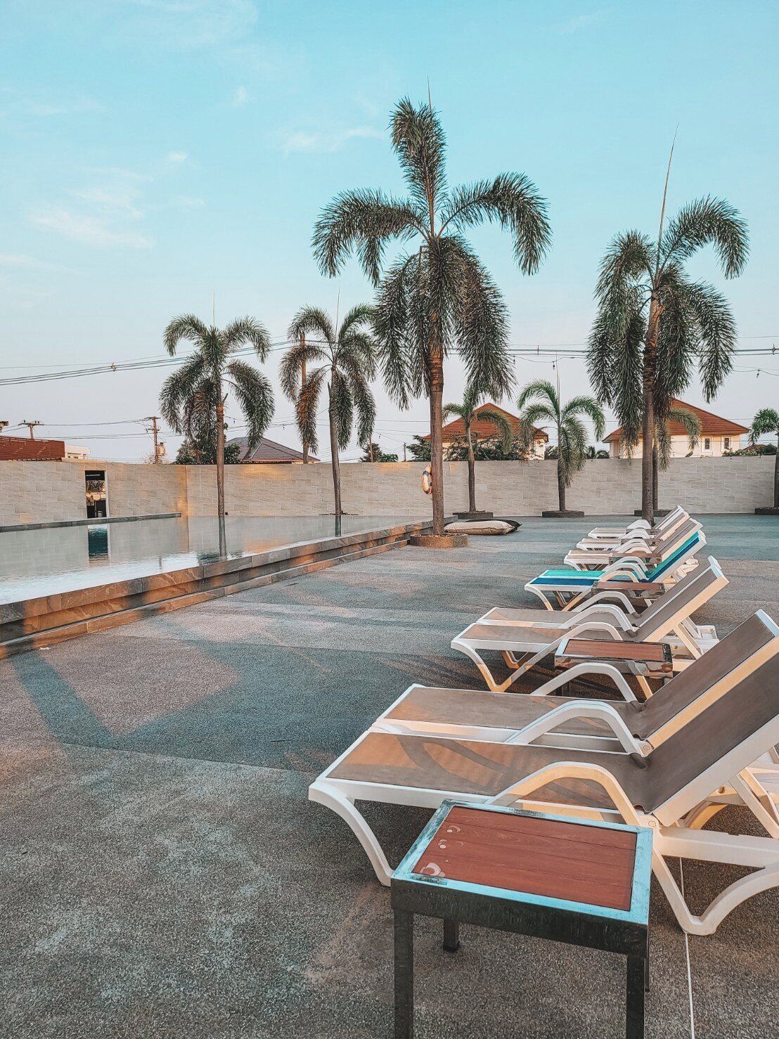 A row of sun loungers with a stone wall and palm trees in the background.