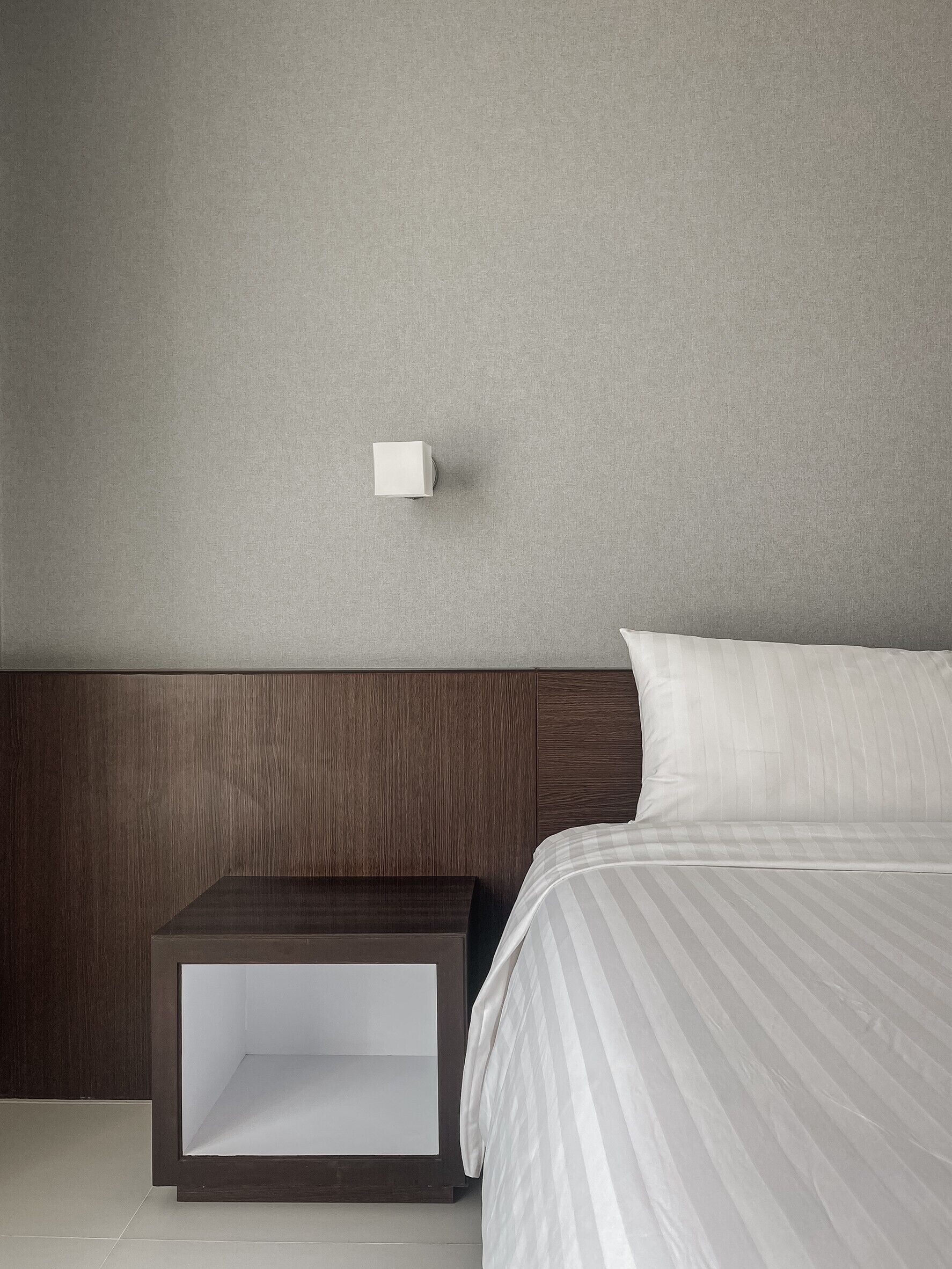 Camera d'albergo moderna con una testiera in legno, un letto a righe bianche e un comodino con una lampada bianca.