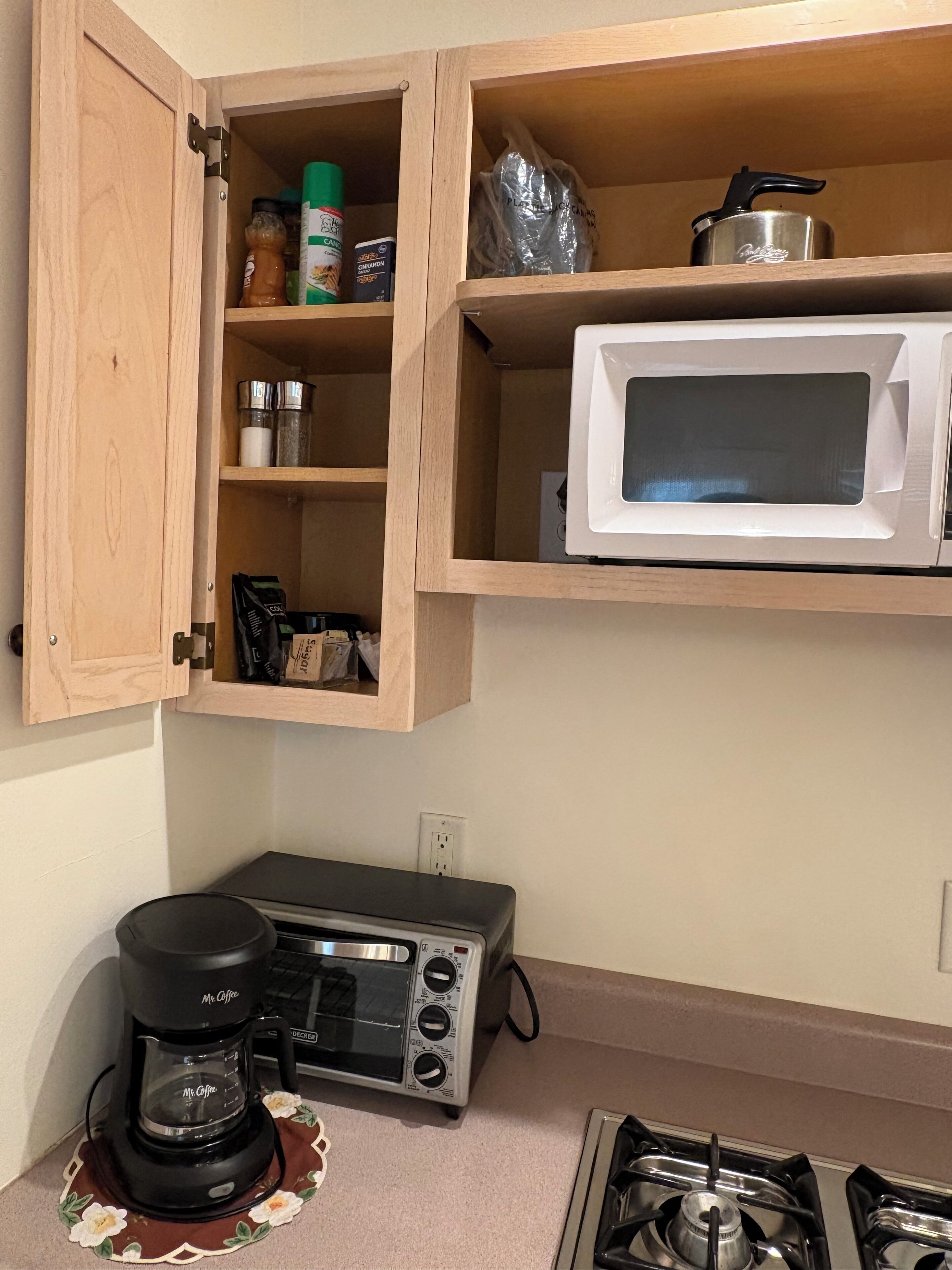 A kitchen with a microwave, coffee maker, and a cabinet with spices.