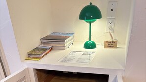 A small room with a white desk, a green desk lamp, a stack of books, and a 'Thank You for Not Smoking' sign. - Room 6️⃣ with kitchen and bathroom in Old Palm Springs hotel by the heated pool 🦋 (Palm Springs)