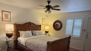 A bedroom with a wooden bed, two bedside tables with lamps, a ceiling fan, and a door with blinds. - Room 6️⃣ with kitchen and bathroom in Old Palm Springs hotel by the heated pool 🦋 (Palm Springs)