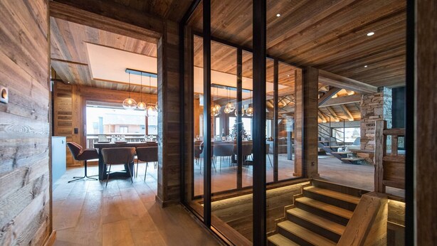 A modern interior with wooden beams, a staircase, and a dining area with tables and chairs. - Luxurious chalet with indoor pool, sauna, and home cinema (LA TOUSSUIRE)