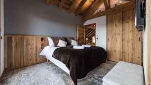 A bedroom with a wooden ceiling, a bed with a dark blanket, a white pillow, and a wooden wardrobe. - Luxurious chalet with indoor pool, sauna, and home cinema (LA TOUSSUIRE)