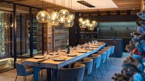 A modern dining area with a long wooden table set for a meal, surrounded by chairs. - Luxurious chalet with indoor pool, sauna, and home cinema (LA TOUSSUIRE)