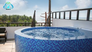 Een hottub met een betegeld blauw interieur, een houten terras en uitzicht op de oceaan en palmbomen.