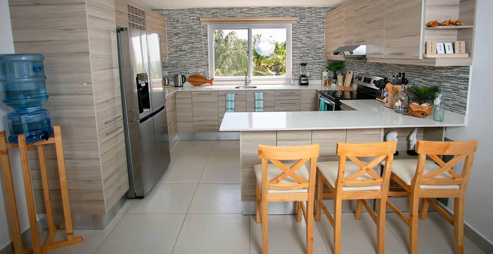 Una cocina moderna con una isla central, sillas de madera, un refrigerador y un dispensador de agua.