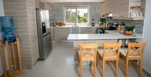 Une cuisine moderne dotée d’un îlot central, de chaises en bois, d’un réfrigérateur et d’un distributeur d’eau.