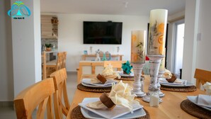 Een eettafel gedekt met borden, servetten en kaarsen, met een televisie op de achtergrond.