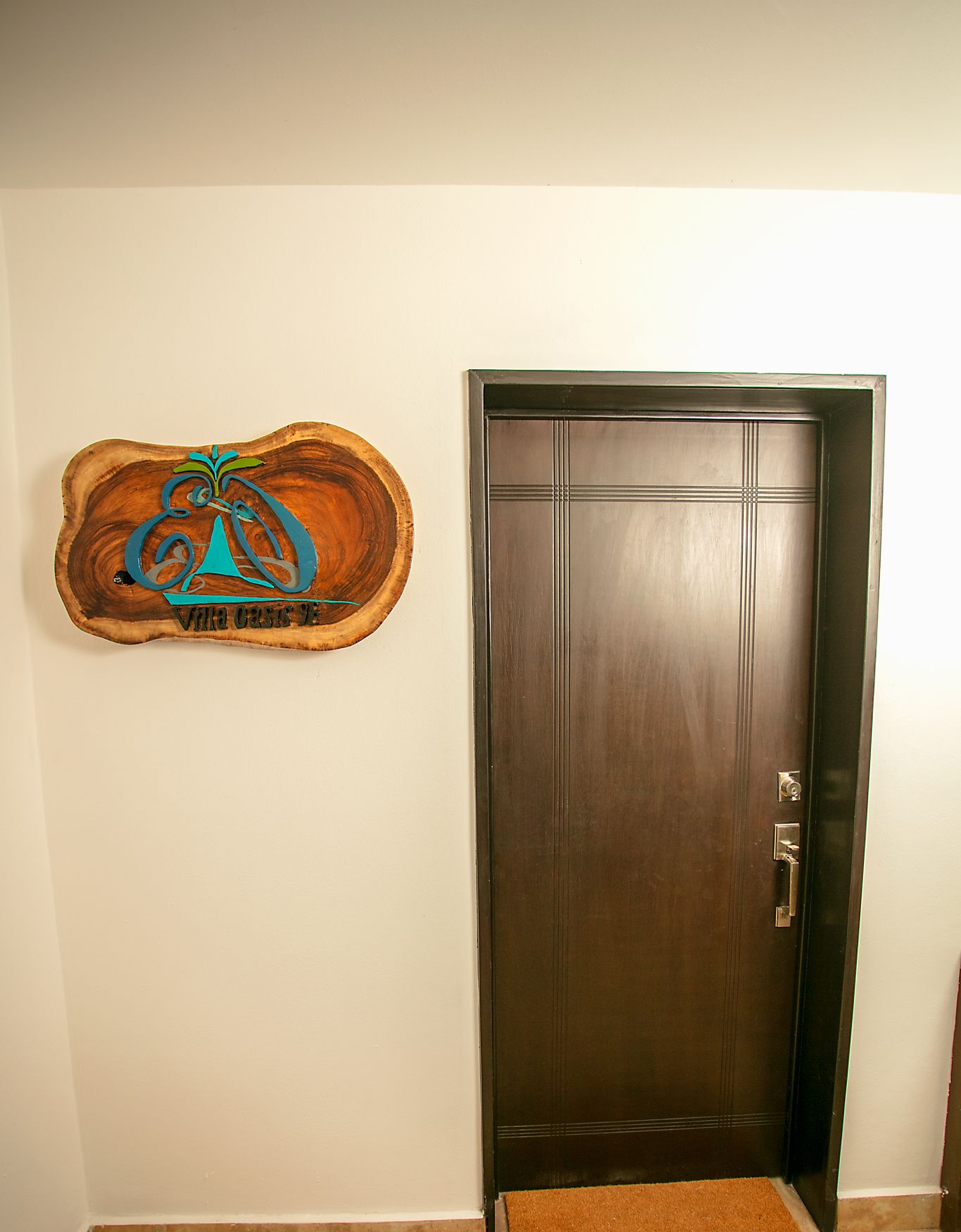 Une porte en bois avec une poignée en métal, un paillasson et un élément décoratif en bois représentant un logo, fixé au mur.