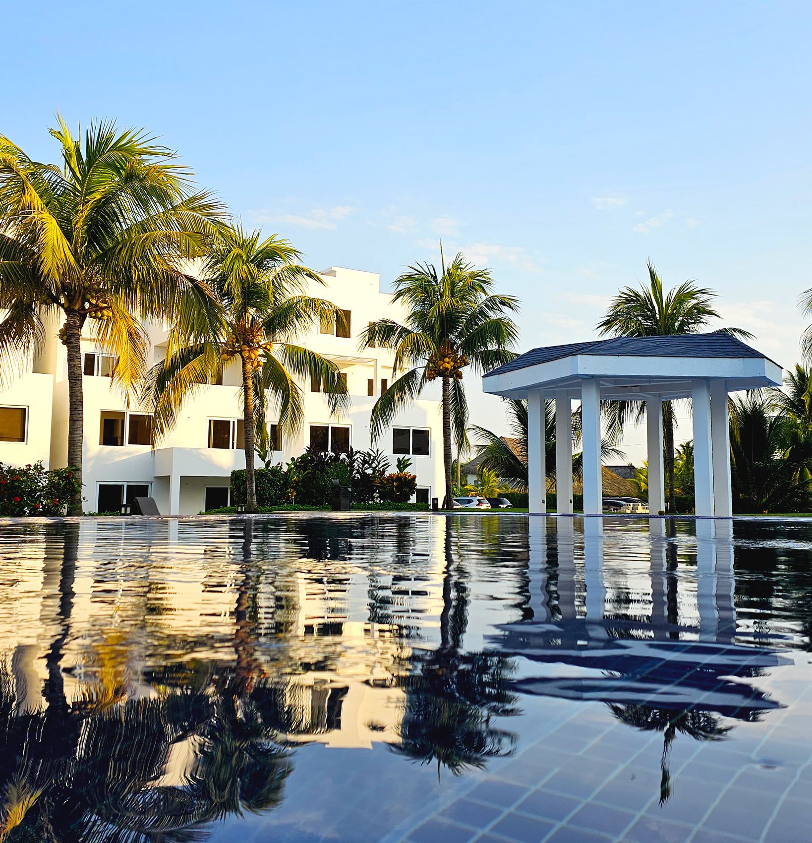 A resort pool with a gazebo, palm trees, and a modern building.