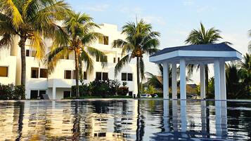 Una piscina de resort con un pabellón, palmeras y un edificio moderno.