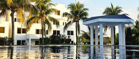 A resort pool with a gazebo, palm trees, and a modern building.