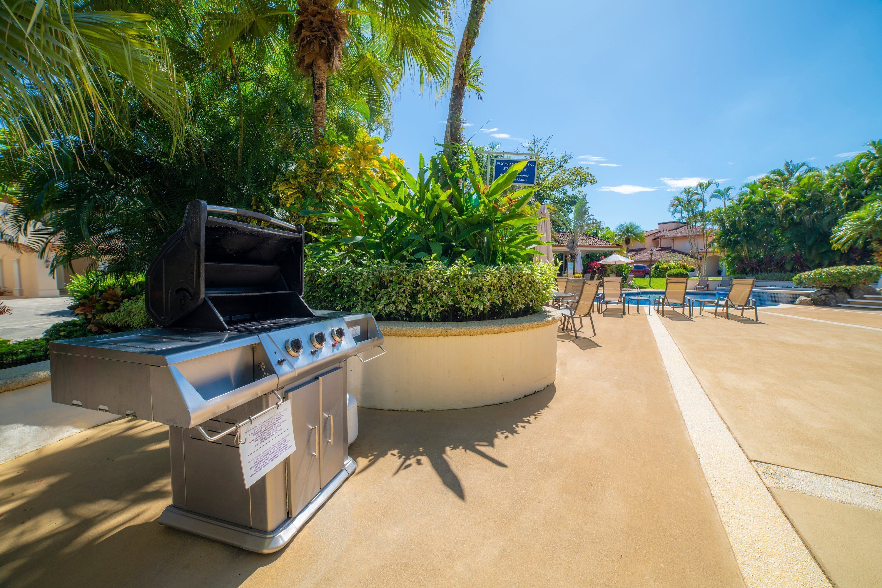 Un espace barbecue extérieur, agrémenté d’un barbecue, entouré d’une végétation luxuriante et surplombé d’un ciel bleu dégagé.