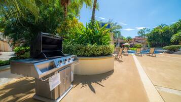 Un espace barbecue extérieur, agrémenté d’un barbecue, entouré d’une végétation luxuriante et surplombé d’un ciel bleu dégagé.
