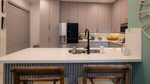Una cocina moderna con gabinetes grises, una isla central con un lavamanos y dos sillas de mimbre.
