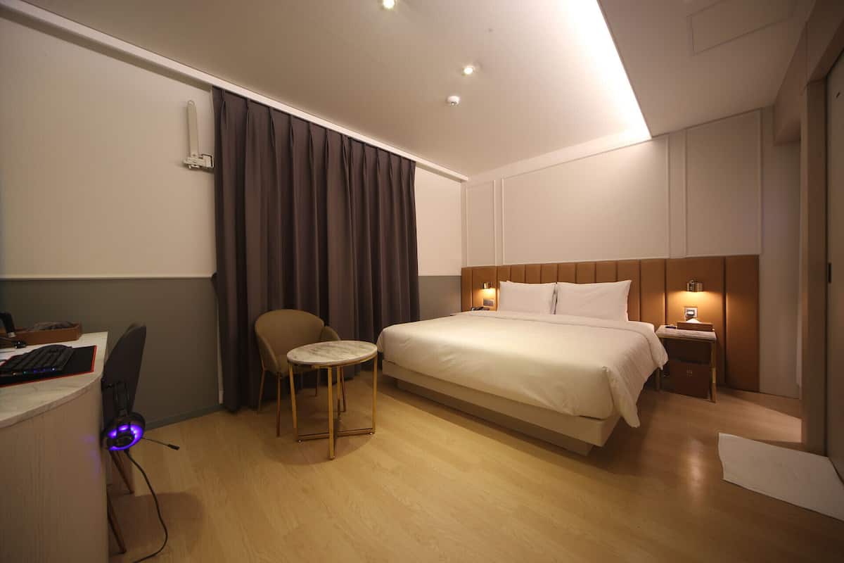 A hotel room with a bed, a desk with a computer, a chair, and a small table.