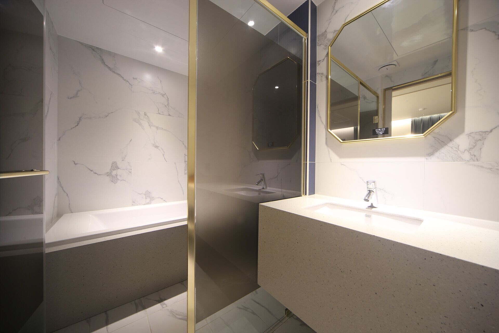Un baño moderno con paredes de mármol, cabina de ducha de vidrio y un espejo grande con marco dorado.