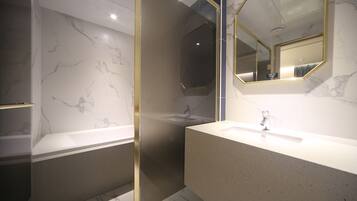 Un baño moderno con paredes de mármol, cabina de ducha de vidrio y un espejo grande con marco dorado.