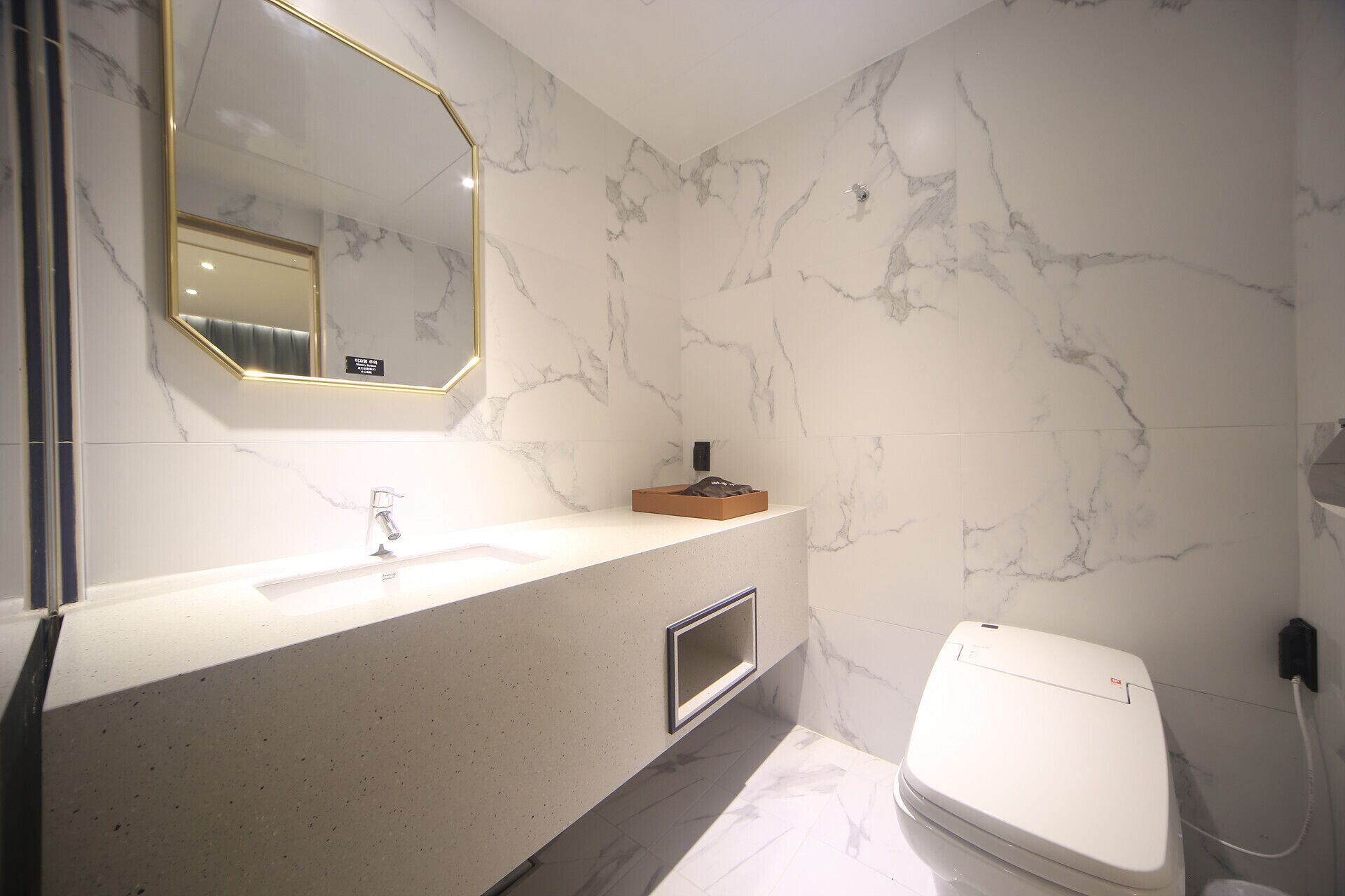 A modern bathroom with a marble wall, a gold-framed mirror, a sink, and a toilet.