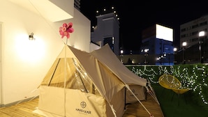 A tented area with a HardGear logo, a wooden deck, and a chair with string lights. - H Avenue Hotel (Busan)