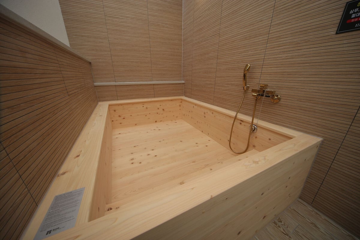 A wooden bathtub with a shower head and controls, surrounded by wooden panel walls.