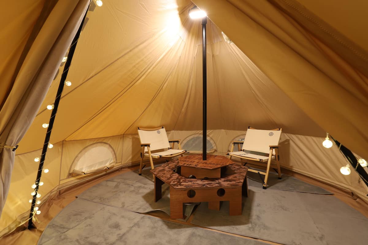 A tent with two chairs and a table, string lights, and a pole with lights.