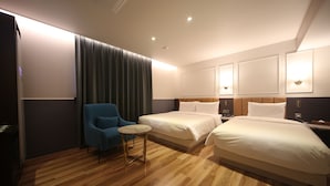 A hotel room with two beds, a small round table, a blue armchair, and a large window with curtains. - H Avenue Hotel (Busan)