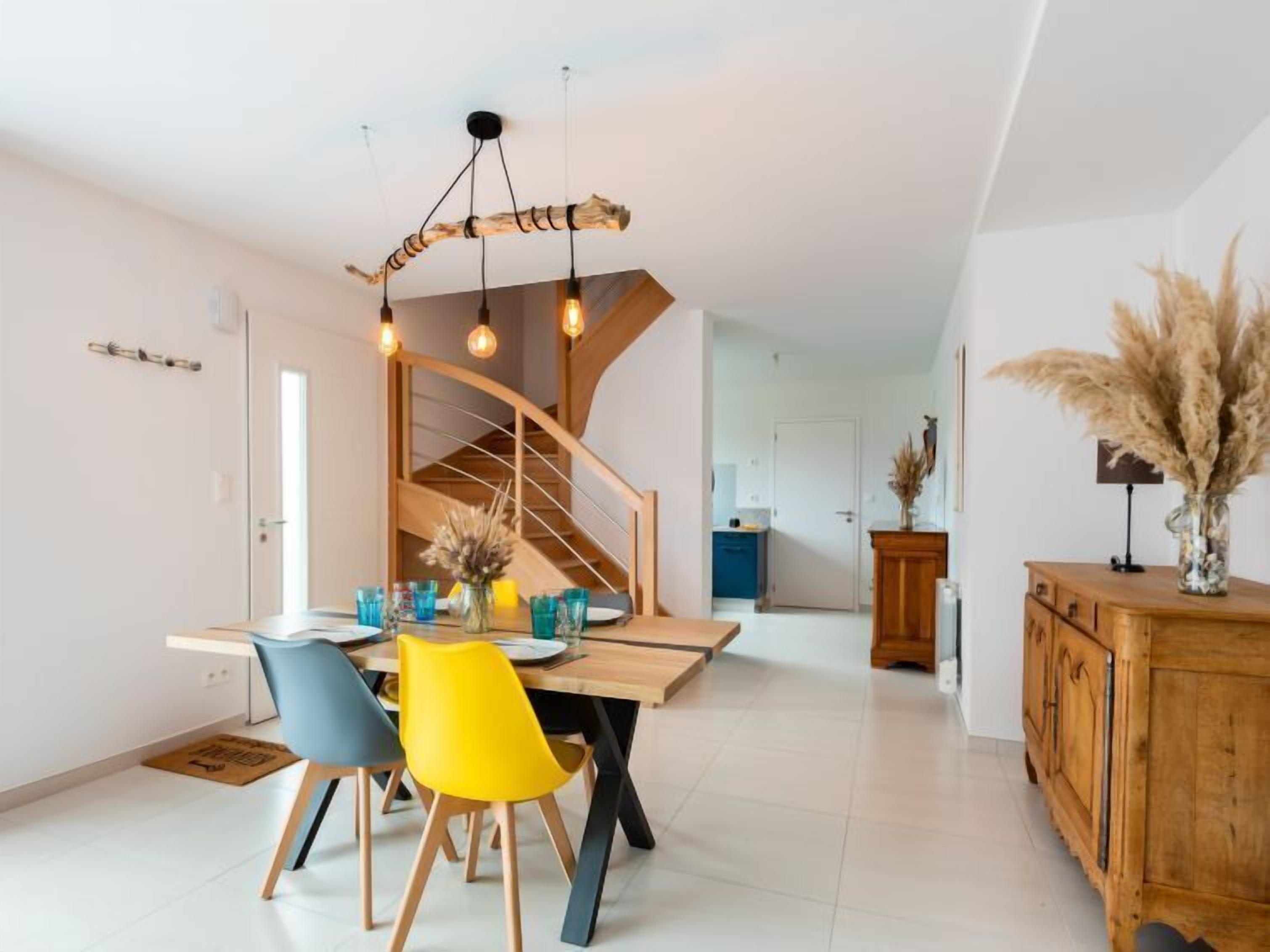 A modern dining area with a wooden table, colorful chairs, and a unique light fixture.
