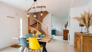 A modern dining area with a wooden table, colorful chairs, and a unique light fixture. - Vacation home Océane by Interhome (Barneville Carteret)