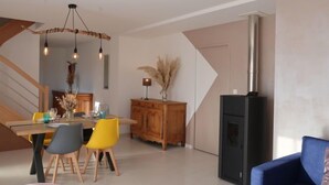 A modern living room with a dining area, a staircase, and a black wood-burning stove. - Vacation home Océane by Interhome (Barneville Carteret)
