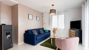 A modern living room with a blue sofa, a pink chair, a small coffee table, a TV, and a fireplace. - Vacation home Océane by Interhome (Barneville Carteret)