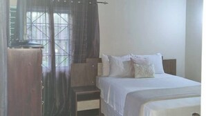 A bedroom with a bed, bedside table, and a window with curtains. - 3-Bed House Sleeps 6 with Mountain Views (Ocho Rios)