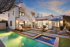 A modern house with a swimming pool, outdoor seating, and a well-lit patio area.