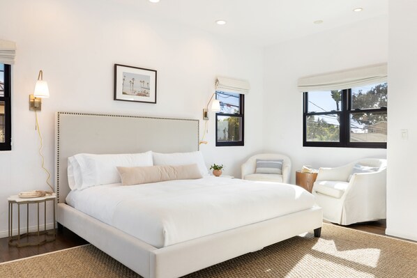A modern bedroom with a large bed, a sitting area with a chair, and a window providing a view of the outdoors.