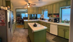 Una cocina con armarios verdes, una isla central, un refrigerador y un lavavajillas.