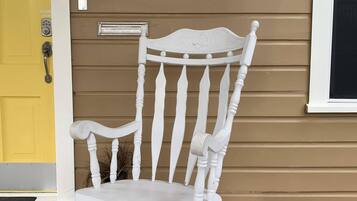 Une chaise berçante blanche est placée devant une maison dont la porte est jaune et sur le mur flotte un drapeau du Texas.