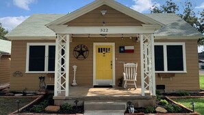 A two-story house with a yellow front door, number 322, and a Texas flag.