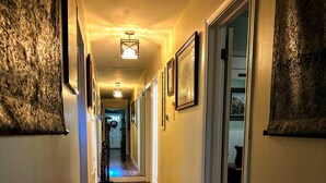 A hallway with wooden flooring, framed pictures on the walls, and a door leading to a room.