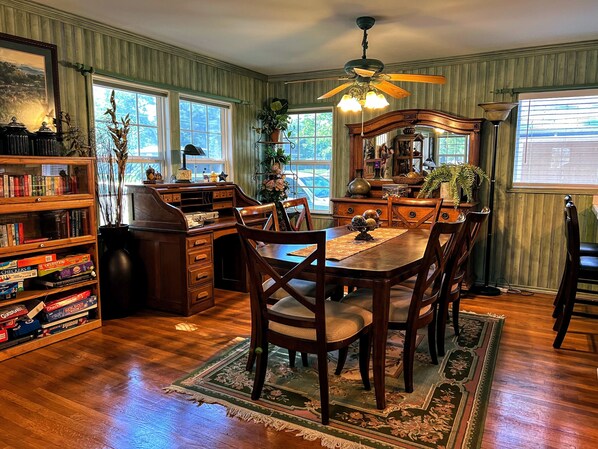 Un comedor con mesa de madera, sillas, una araña y una estantería llena de libros.