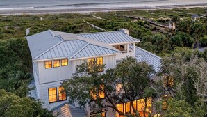 A modern house with a metal roof, surrounded by lush greenery and overlooking a beach. - Discounts! OCEANFRONT STUNNER- Discounted Rates! Pool, Hot Tub, Elevator (Isle Of Palms)