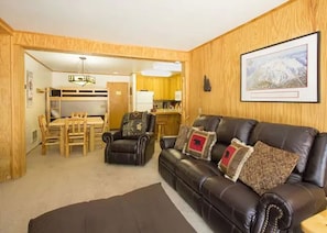A cozy living room with a leather sofa, a dining table with chairs, and a kitchen area visible through an open doorway. - Ski in/ski out across from Austria Hof (Mammoth Lakes)