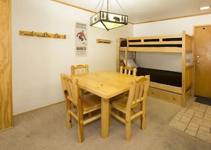 A room with a bunk bed, a wooden table with chairs, a hanging light fixture, and a poster on the wall. - Ski in/ski out across from Austria Hof (Mammoth Lakes)