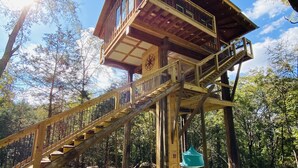 A wooden tower with a staircase leading up to a balcony, surrounded by trees and a clear sky. - 1 bed 1 bath Treehouse called the Firetower (Jackson)