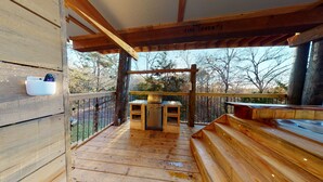 A wooden deck with a hot tub, a grill, and a wooden bench. - 1 bed 1 bath Treehouse called the Firetower (Jackson)