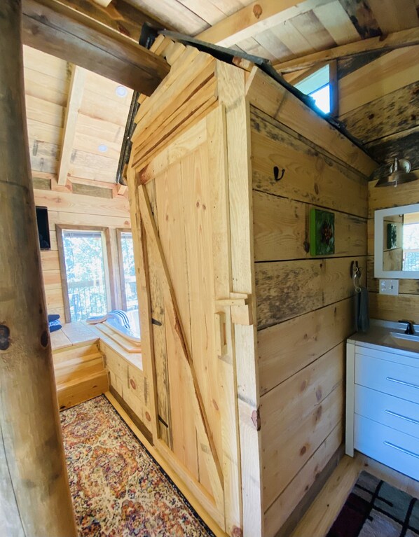 Interior de una cabaña de madera con una puerta grande de madera, una ventana pequeña, un lavabo y una alfombra estampada.